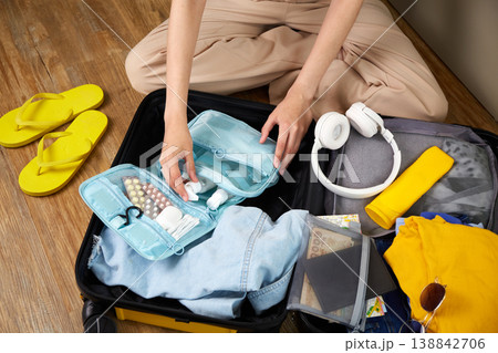 A woman puts hygiene products, clothes, a travel guide, headphones and travel accessories in a suitcase A woman puts hygiene products, clothes, a travel guide, headphones and travel accessories in a suitcase 138842706