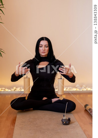 Sound therapy. Relaxing process. Woman doing ritual with traditional wind chime instrument on meditation session in balance pose in studio. Sound therapy. Relaxing process. Woman doing ritual with traditional wind chime instrument on meditation session in balance pose in studio. 138843309