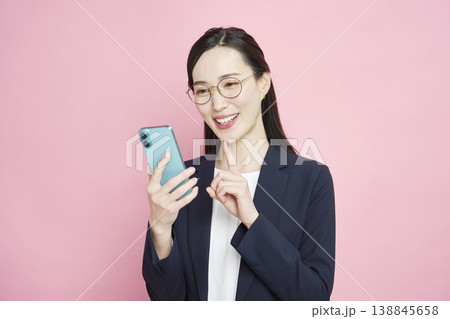 スマホを見て笑顔のビジネスウーマン ピンク背景 スマホを見て笑顔のビジネスウーマン ピンク背景 138845658