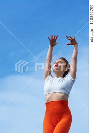 Young woman in bright sportswear stretching arms up to a clear blue sky Young woman in bright sportswear stretching arms up to a clear blue sky 138845794