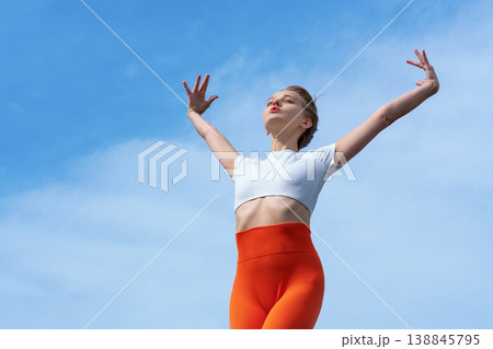 Athletic woman with arms raised in freedom against clear blue sky Athletic woman with arms raised in freedom against clear blue sky 138845795