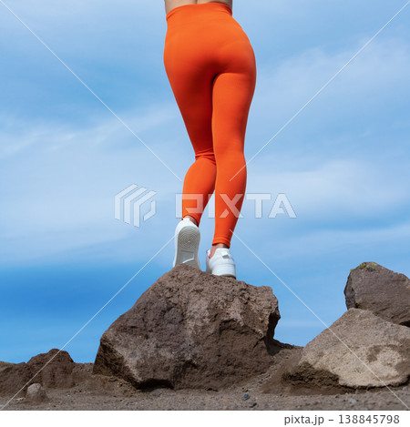 Woman's legs in bright orange activewear standing rock against blue sky 138845798