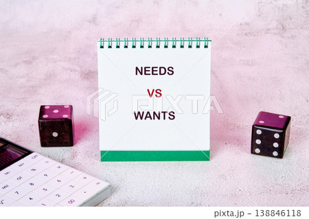 White notepad displays NEEDS VS WANTS text on a pink surface 138846118
