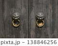 Pair of Antique Brass Lion Head Door Knockers on Weathered Wooden Double Doors 138846256