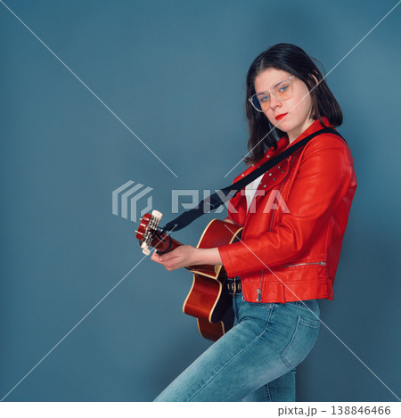Confident young woman in red jacket holding an acoustic guitar 138846466