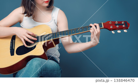 Female musician playing chords on an acoustic guitar against blue background 138846470