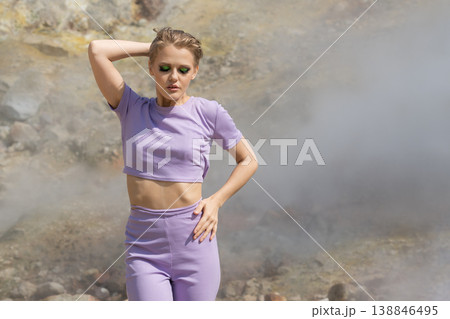 Stylish woman in lavender outfit with bold green eyeshadow posing in a surreal, steamy landscape Stylish woman in lavender outfit with bold green eyeshadow posing in a surreal, steamy landscape 138846495