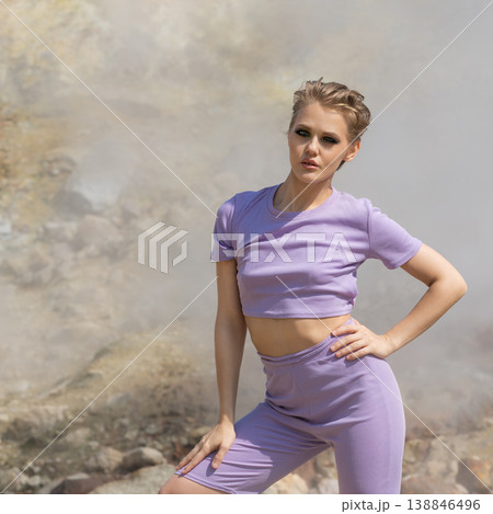 Confident woman with short hair in purple athleisure outfit posing in a steamy, rocky landscape Confident woman with short hair in purple athleisure outfit posing in a steamy, rocky landscape 138846496