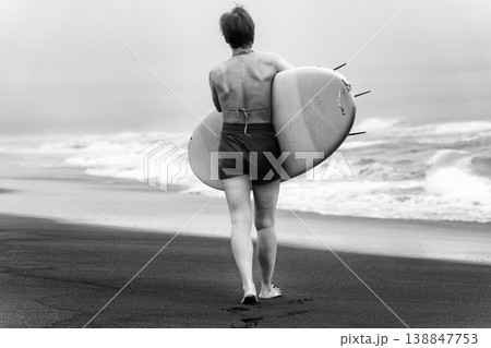 Black and white rear view of female surfer carrying surfboard and walking on beach Black and white rear view of female surfer carrying surfboard and walking on beach 138847753