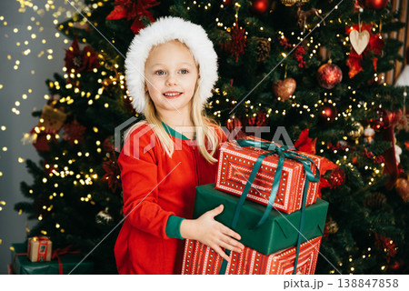 Merry Christmas and Happy Holidays. Little child under Christmas tree. baby girl in Santa Claus hat with gifts under Christmas tree with many gift boxes presents. Happy Holidays, New year. Merry Christmas and Happy Holidays. Little child under Christmas tree. baby girl in Santa Claus hat with gifts under Christmas tree with many gift boxes presents. Happy Holidays, New year. 138847858