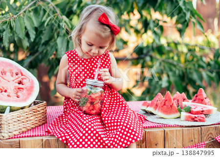 Cute child eats ripe juicy watermelon at summertime. Child, baby, healthy food snack for children. Adorable little girl trying to sell lemonade. Watermelon lemonade with ice and mint 138847995