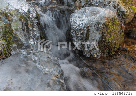 Frozen branches at edge of flowing stream during winter in forest Frozen branches at edge of flowing stream during winter in forest 138848715