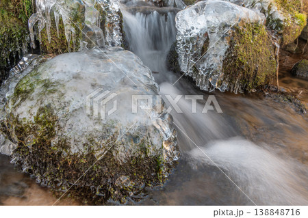 Frozen branches at edge of flowing stream during winter in forest 138848716
