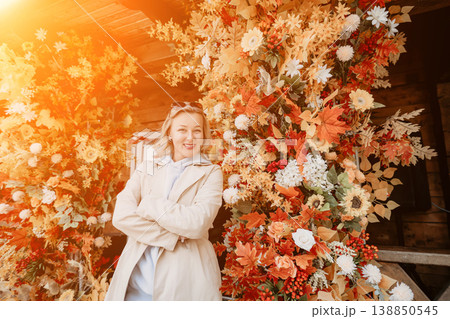 Woman in Beige Coat Posing in Front of Autumnal Floral Decorations 138850545