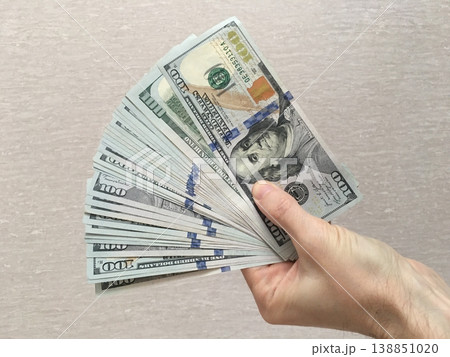 Hand holding a stack of hundred dollar bills against a simple background 138851020