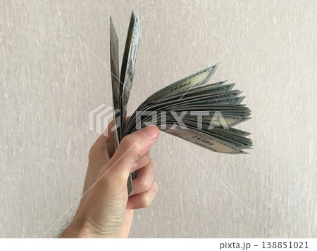 Hand holding fan of cash with more bills sticking out in front of plain background during daytime Hand holding fan of cash with more bills sticking out in front of plain background during daytime 138851021