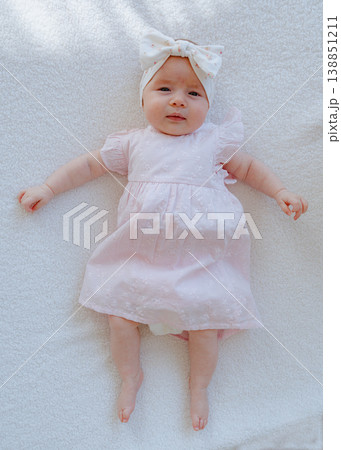 Baby girl in pink dress lying on soft white surface. Minimal full body composition with clean background and copy space. Baby girl in pink dress lying on soft white surface. Minimal full body composition with clean background and copy space. 138851211