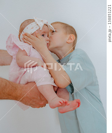 Young boy gently kissing baby girl in tender family moment. Love, care, and sibling bonding at home. Authentic lifestyle scene with soft natural light. 138851221