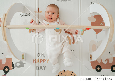 Cute baby resting on play mat under activity gym toys. Concept of parenting, infant learning and childhood playtime. Cute baby resting on play mat under activity gym toys. Concept of parenting, infant learning and childhood playtime. 138851223
