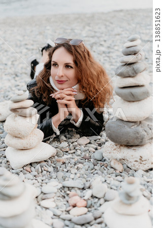 Woman beach relaxation Woman lying on pebble beach beside stacked stone cairns during peaceful coastal vacation 138851623