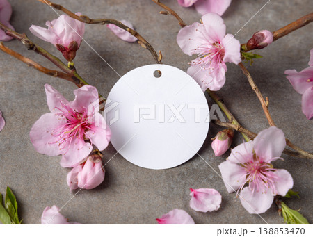 Blank round gift tag mockup with pink spring flowers and wooden twigs on grey stone, label design 138853470