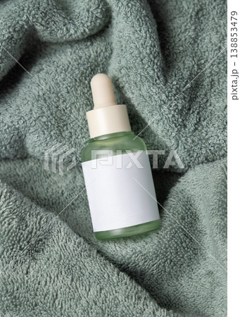 Glass dropper bottle with blank label mockup on sage green bath towel, unbranded packaging 138853479