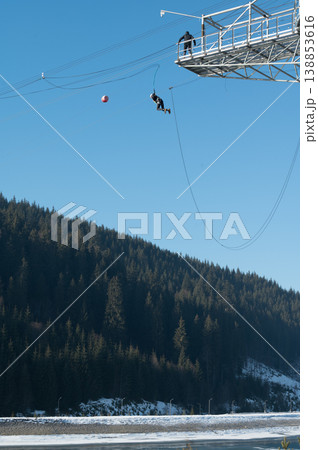 Adventurer descends from a towering structure into serene winter landscape while enjoying thrilling experience over snow-capped terrain Adventurer descends from a towering structure into serene winter landscape while enjoying thrilling experience over snow-capped terrain 138853616