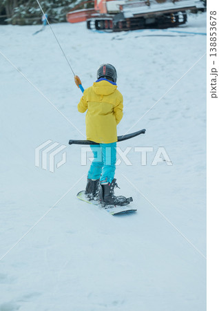 Young skier in bright yellow jacket navigates snowy slopes during winter afternoon, joyfully enjoying a fun day of winter sports activity with friends nearby 138853678