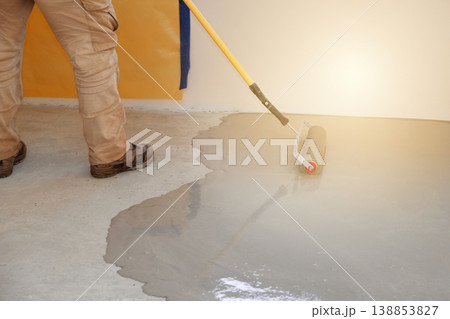 Worker applies concrete coating to a self-leveling floor using a roller in a construction site in the morning time 138853827