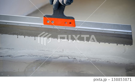 Worker levels concrete using a trowel at a construction site during day hours 138853871