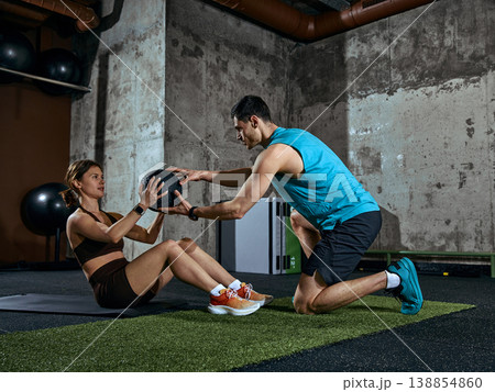 Personal trainer assisting woman with medicine ball during core workout session. Personal trainer assisting woman with medicine ball during core workout session. 138854860