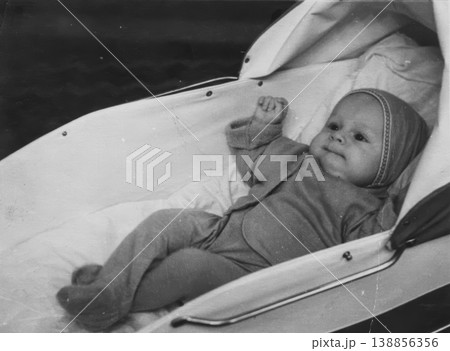 Vintage baby in bonnet lying in pram outdoors 1950s Vintage baby in bonnet lying in pram outdoors 1950s 138856356