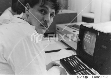 Young man in lab coat working at vintage computer terminal 1980s Young man in lab coat working at vintage computer terminal 1980s 138856398