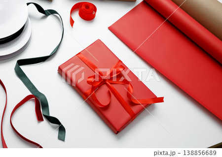 Wrapped gift in red paper tied with satin ribbon for holiday celebration giving Wrapped gift in red paper tied with satin ribbon for holiday celebration giving 138856689