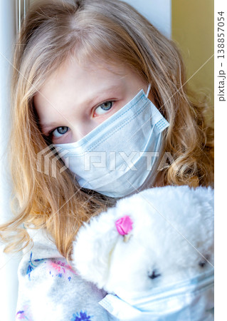girl in medical mask with teddy bear, looking out the window, quarantine coronavirus. sick children 138857054
