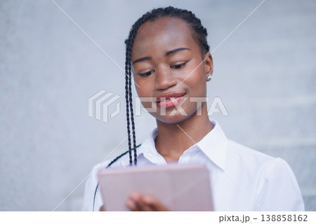 Close portrait of young Black woman looking at a tablet with a soft smile. Digital reading, online learning, remote work, mobile communication and modern technology lifestyle. Close portrait of young Black woman looking at a tablet with a soft smile. Digital reading, online learning, remote work, mobile communication and modern technology lifestyle. 138858162