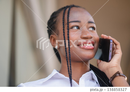 Close up of young Black business woman smiling during smartphone call outdoors, looking away with confidence. Mobile communication, customer service, remote work and modern lifestyle concept. 138858327