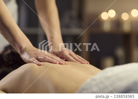 Therapist hands massaging back in spa with warm candles and calming ambiance Therapist hands massaging back in spa with warm candles and calming ambiance 138858365