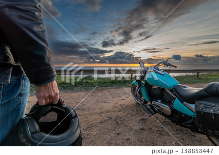 Biker with a helmet on his hand stands by a motorcycle 138858447