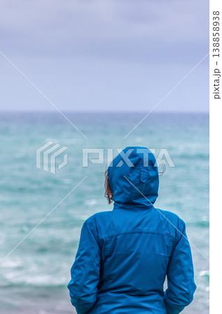 Vertical View of Woman in Hiking Jacket Watching Stormy Sea, Waist-Up Rear View Vertical View of Woman in Hiking Jacket Watching Stormy Sea, Waist-Up Rear View 138858938