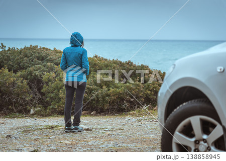 Woman in Hiking Clothes Watching Stormy Sea with SUV Detail in Foreground Woman in Hiking Clothes Watching Stormy Sea with SUV Detail in Foreground 138858945