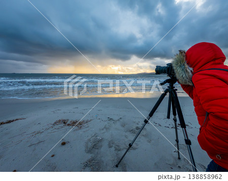 Female Photographer Looking Through DSLR Viewfinder on Tripod on Beach at Sunset Female Photographer Looking Through DSLR Viewfinder on Tripod on Beach at Sunset 138858962