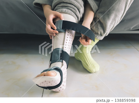 Hands adjust the strap on a patient's light pink perforated medical foot and ankle brace Hands adjust the strap on a patient's light pink perforated medical foot and ankle brace 138859398