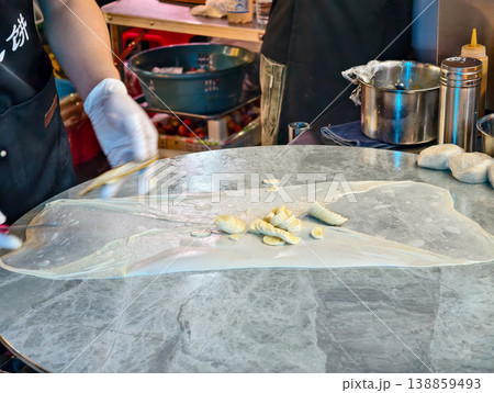 Artisan preparing fresh pancake wrappers with precision on a marble countertop in a bustling street food market Artisan preparing fresh pancake wrappers with precision on a marble countertop in a bustling street food market 138859493