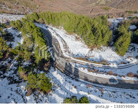 Mountain Road surrounded by snow Viewed from Above with Green Pine Trees and Two Cars 138859886
