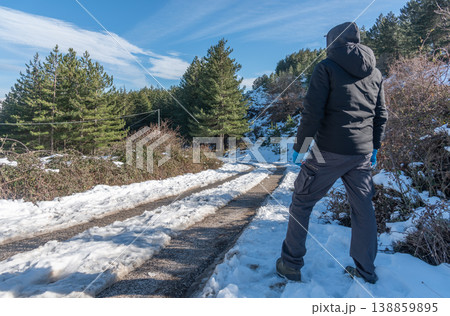 Man Seen from Behind Standing on Snowy Mountain Road Under Blue Sky 138859895