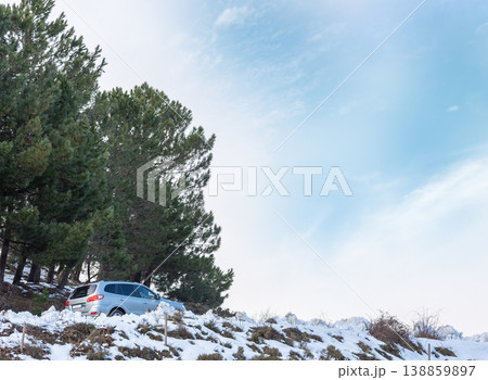 SUV on a Mountain Road Surrounded by Snow Under a Blue Sky with Clouds 138859897