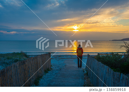 Woman Standing on Beach Path at Sunset with Calm Sea and Clouds 138859918