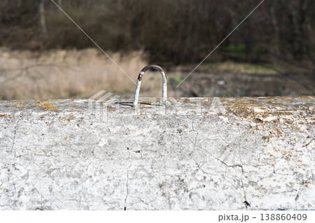 Close-up of a weathered concrete block with a rusty metal lifting loop against a blurred nature background. Close-up of a weathered concrete block with a rusty metal lifting loop against a blurred nature background. 138860409