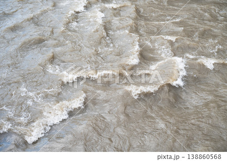 Turbulent brown water of a muddy river during a flood or heavy rain.  Rapid flow of muddy floodwater with ripples and small waves. 138860568